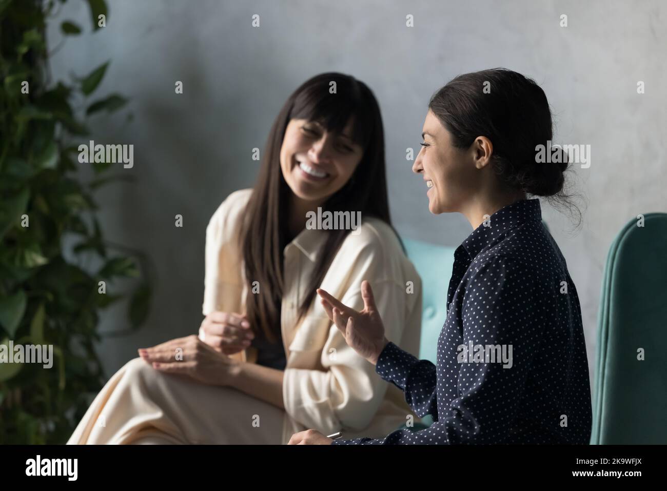 Zwei fröhliche, multiethnische Frauen, die drinnen sitzen und lachen Stockfoto
