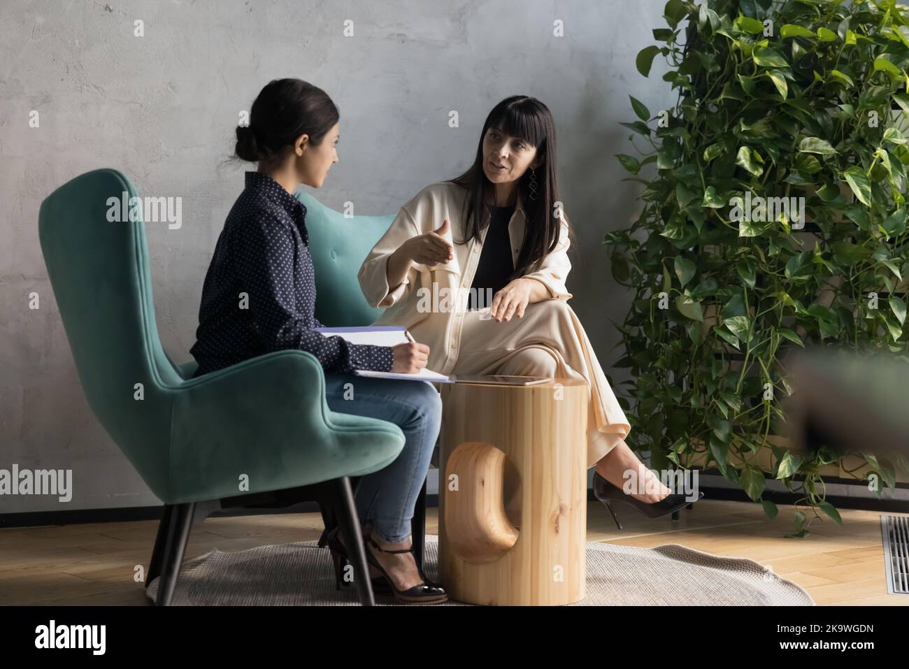 Eine Geschäftsfrau mittleren Alters spricht mit einem Praktikanten, der im Büro auf Sesseln sitzt Stockfoto
