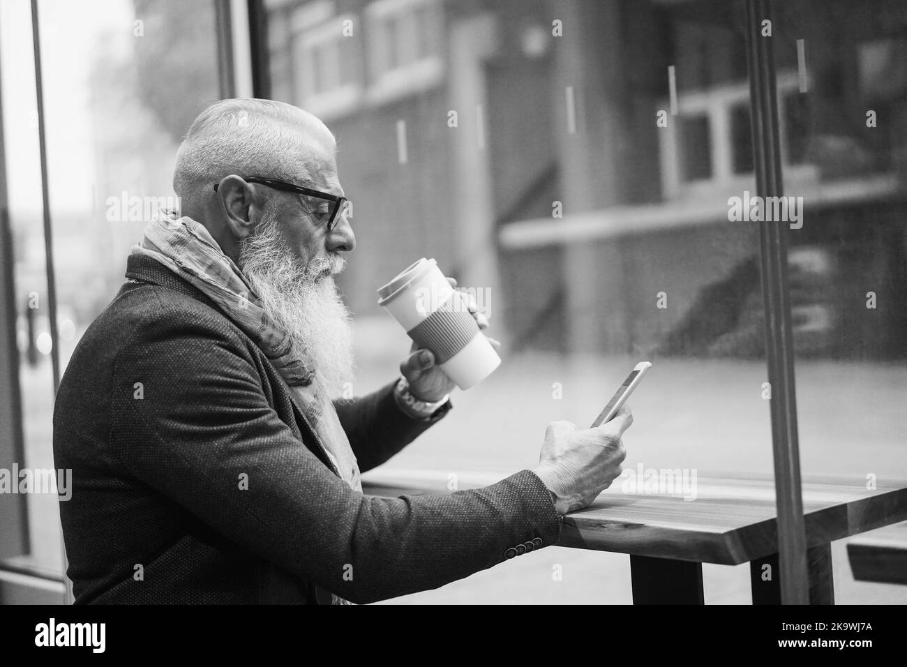 Leitender Geschäftsmann, der in der Café-Bar Kaffee trinkt, mit dem Mobiltelefon – Hauptaugenmerk liegt auf dem Männerohr – Schwarzweißschnitt Stockfoto