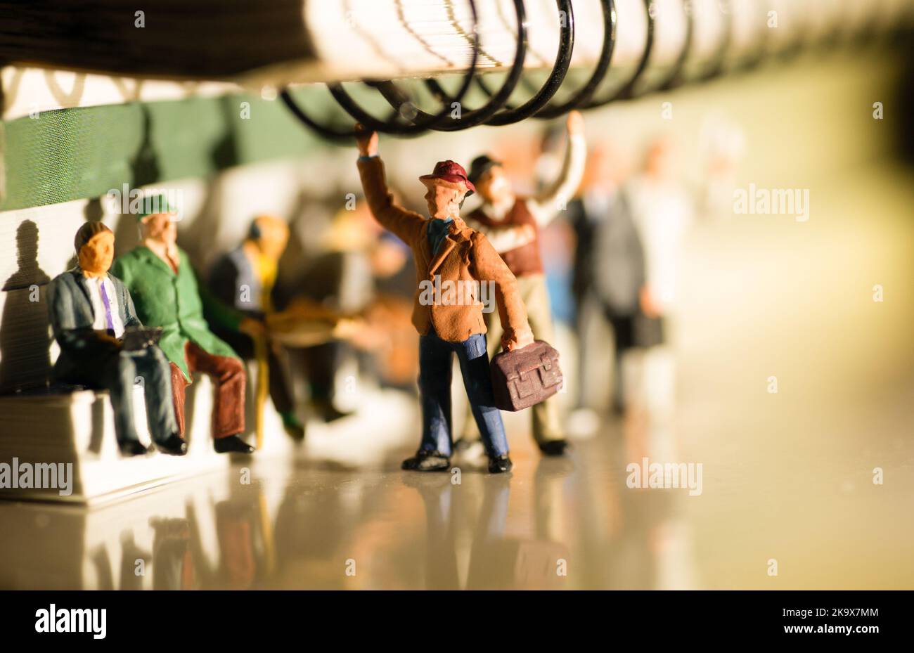 Miniaturspielzeug von Personen, die von der Arbeit an einem öffentlichen Verkehrskonzept mit abendlicher gelblicher Seitenbeleuchtung reisen - Reisen Sie mit dem Zug oder Bus. Stockfoto