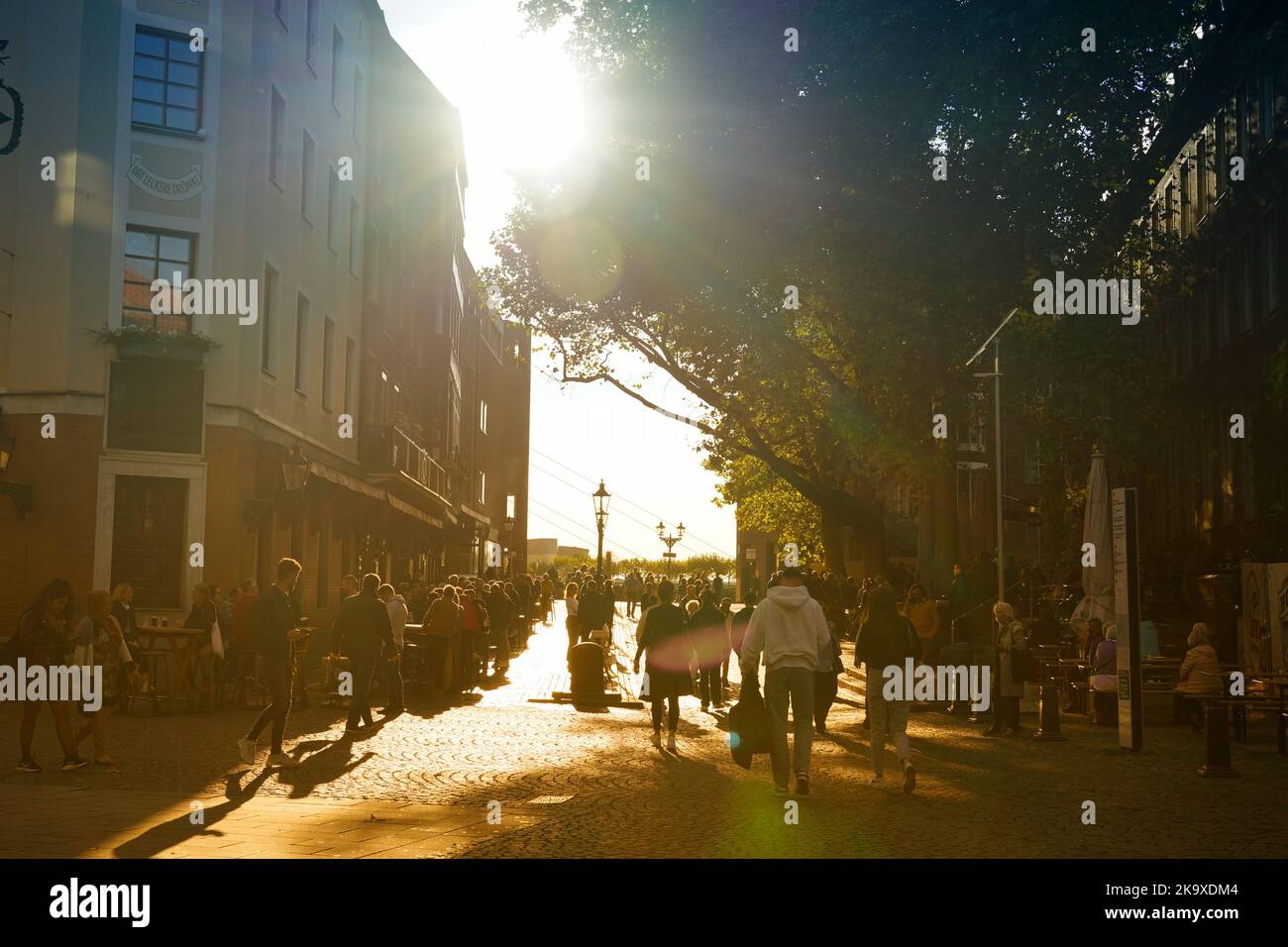 Hintergrundbeleuchtetes Szenenbild einer Kopfsteinpflasterstraße, die zum Rhein Rhiver in der historischen Düsseldorfer Altstadt führt. Am späten Nachmittag Herbstsonne. Stockfoto