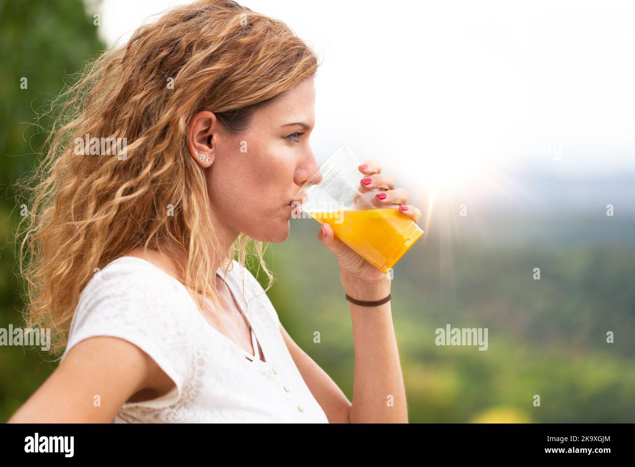 Junge Frau mit lockigen Haaren, die morgens frischen Saft im Freien trinkt, Profilansicht Stockfoto