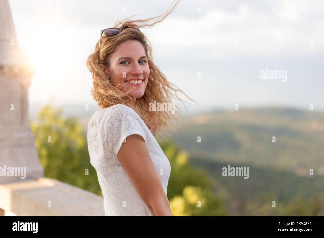 Glückliche junge kaukasische Frau mit lockigen Haaren, die bei Sonnenuntergang im Freien lächelt Stockfoto