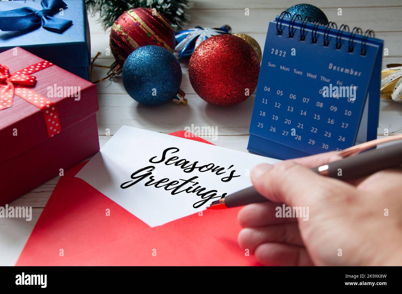 Weihnachtsgrüße auf Notizblock in einem roten Umschlag mit Weihnachtsdekoration und Geschenken im Hintergrund geschrieben. Weihnachtsfeier Stockfoto
