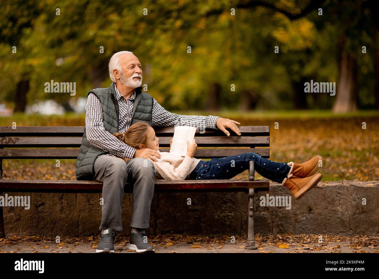Der gutaussehende Großvater verbringt am Herbsttag Zeit mit seiner Enkelin auf der Bank im Park Stockfoto