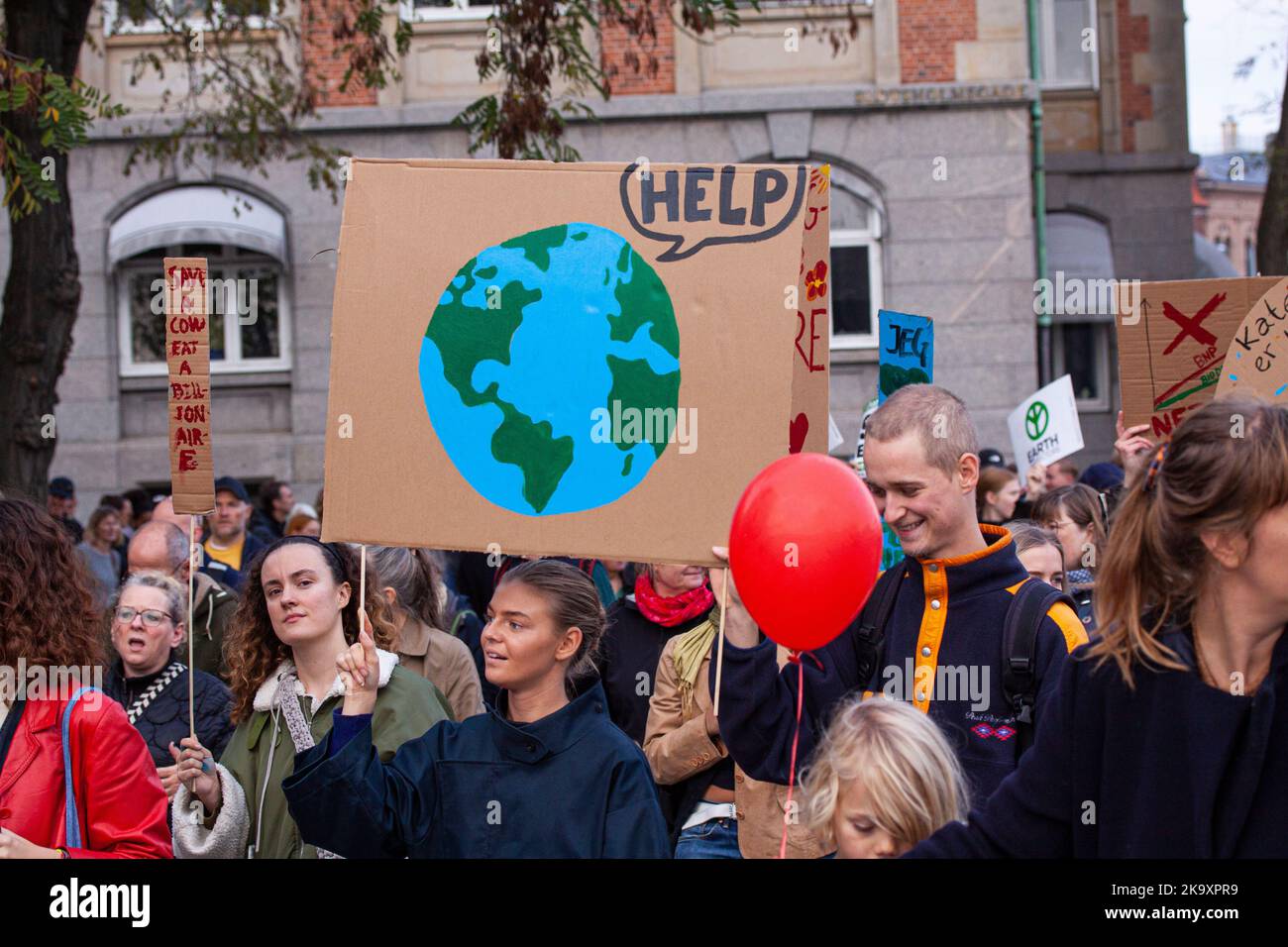 Junge Frau mit einem Schild mit einer Karikatur der Erde, die Hilfe in der Sprechblase sagt. Der Volksklimarsch zur Unterstützung von Maßnahmen auf g Stockfoto