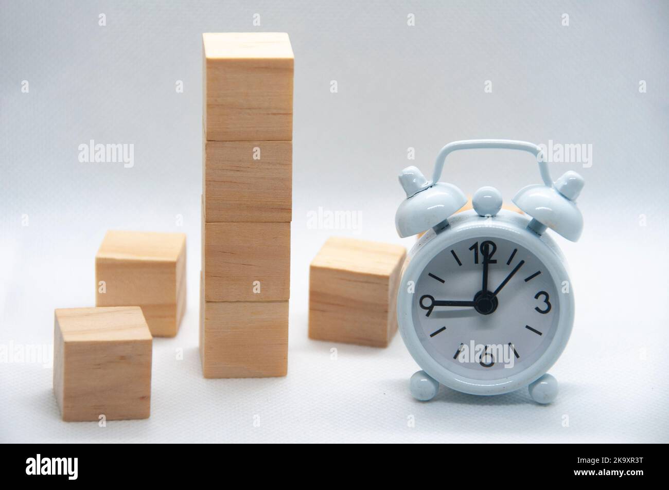 Leere Holzwürfel und weißer Wecker auf weißem Hintergrund mit anpassbarem Platz für Text oder Ideen. Stockfoto
