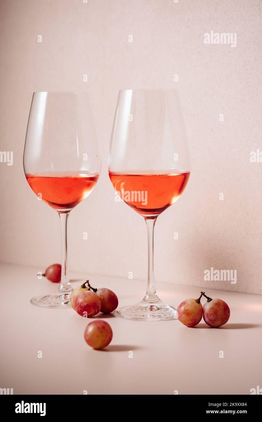 Zwei Gläser Roséwein und rote Trauben auf farbigem Hintergrund. Stockfoto