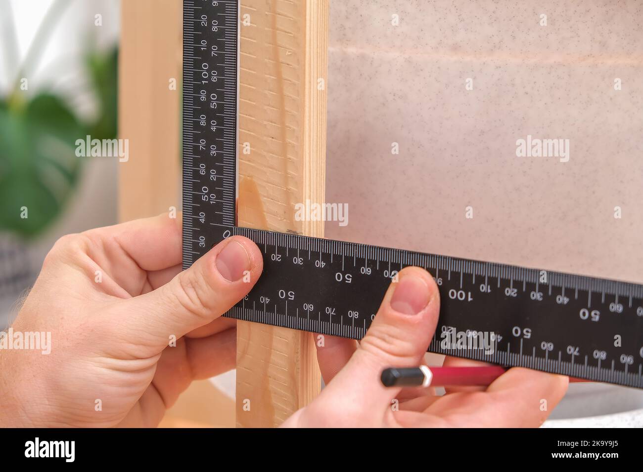 Zimmermann mit Tischlerquadrat, um die Linie von Holz geschnitten für die Konstruktion mit einem Bleistift zu markieren. Eine Nahaufnahme der Hände des Zimmermeisters markiert mit Bleistift und einem Tischlerquadrat auf einem Holzbrett. DIY Stockfoto