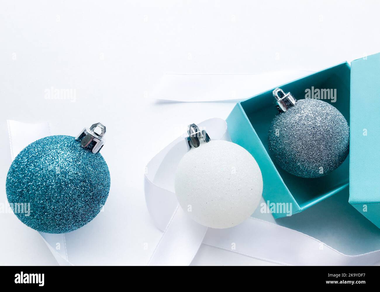 Nahaufnahme von glänzenden Weihnachtskugeln blau türkis, weiß und silber Farbe mit Band auf weißem Hintergrund. Das Konzept von Weihnachten und Feiertagsabend. Stockfoto