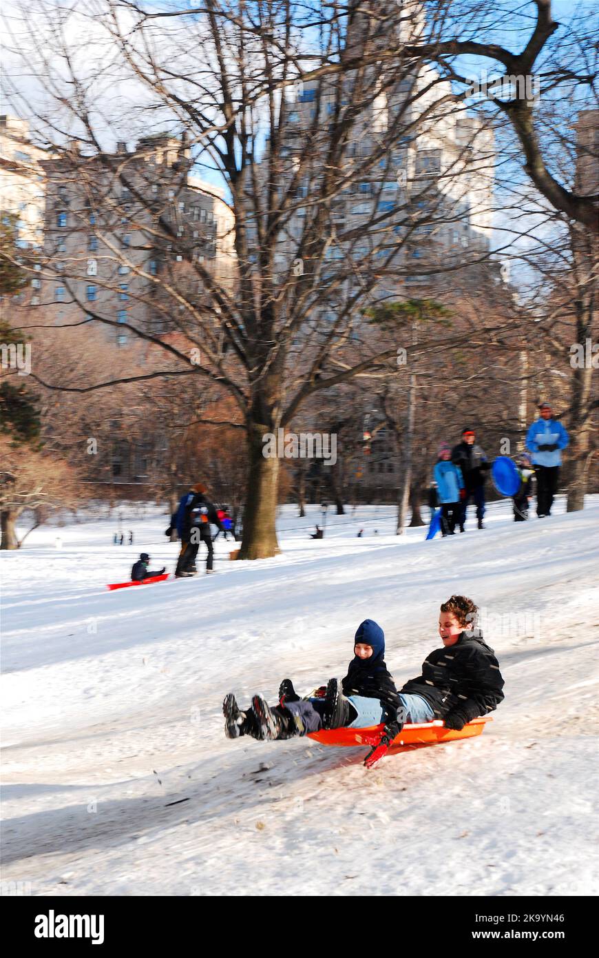 Ein Vater und ein Sohn genießen die gemeinsame Zeit mit der Familie an einem Schneetag und fahren auf dem Pilgrim Hill im Central Park von New York City Stockfoto