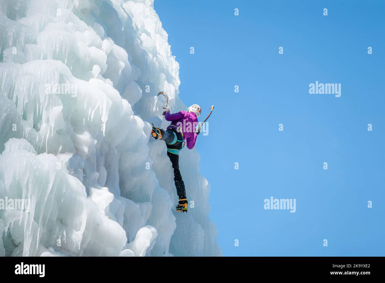 Alpinistin mit Eiskletterausrüstung an einem gefrorenen Wasserfall Stockfoto