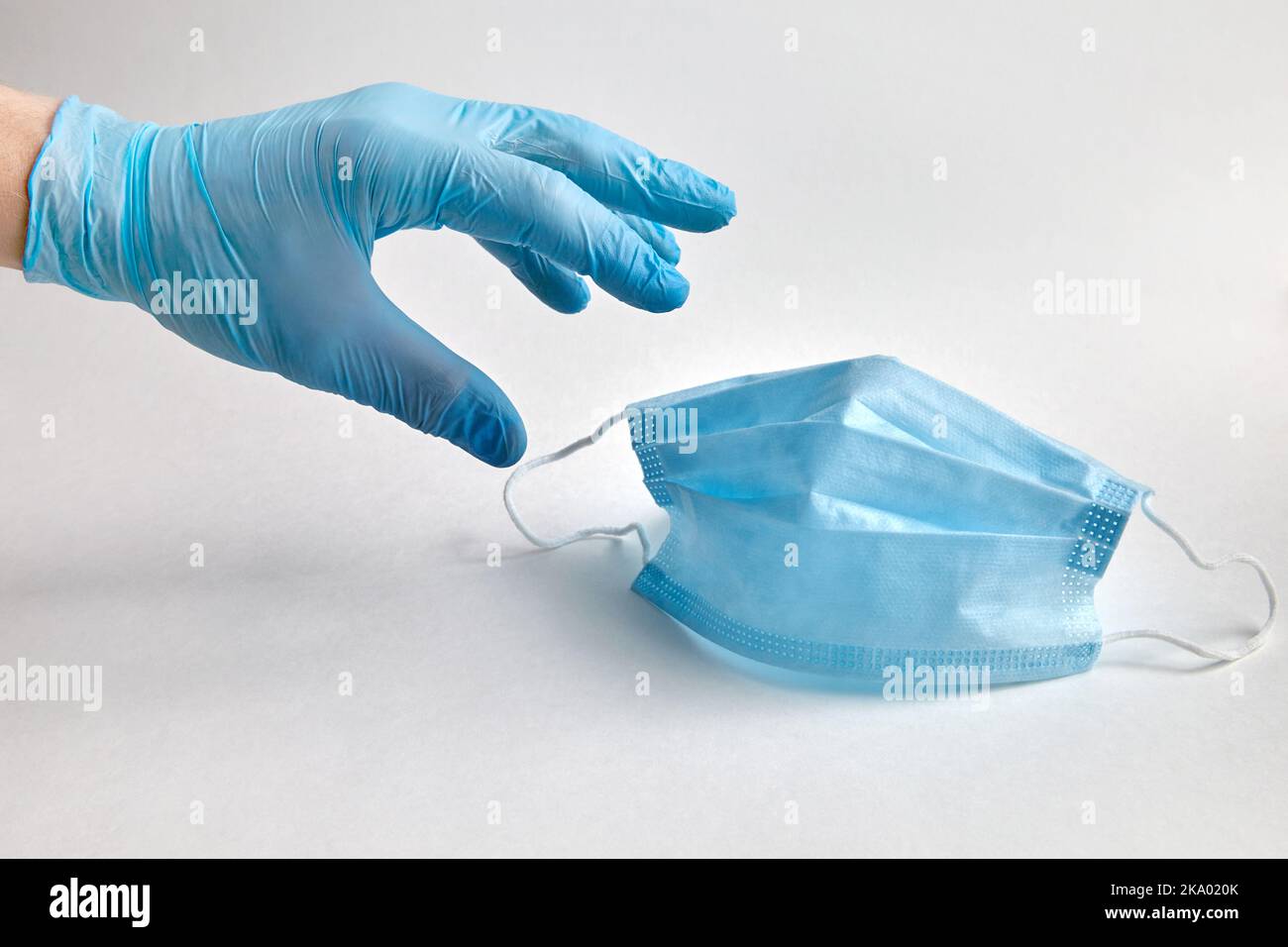 Eine Person in einem blauen Schutzhandschuh greift nach einer schützenden medizinischen Maske. Mittel zum antiviralen und antibakteriellen Schutz Stockfoto