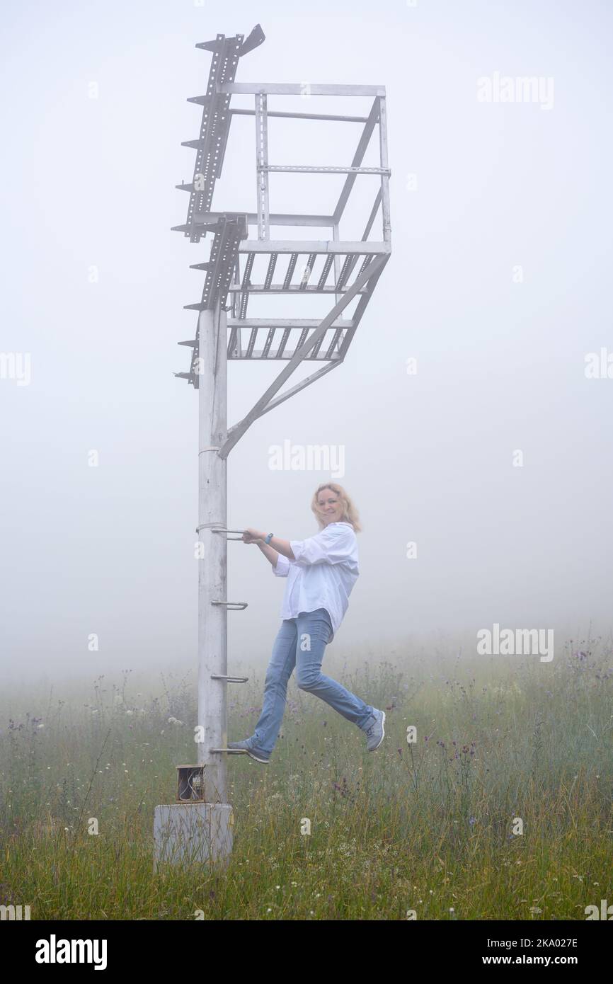 Junge Frau, die Spaß im Nebel, Pyatigorsk, Region Stawropol, Russland. Mädchen klettert und hängt an alten Baustellen am nebligen Maschuk Berg. Wandern, neblig Stockfoto