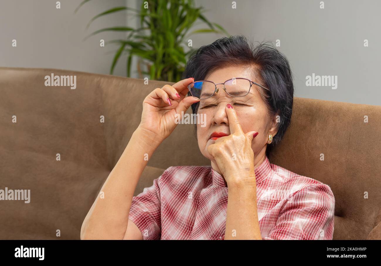 Ältere asiatische Frau, die eine Brille auszieht und an einem Syndrom mit trockenen Augen leidet Stockfoto
