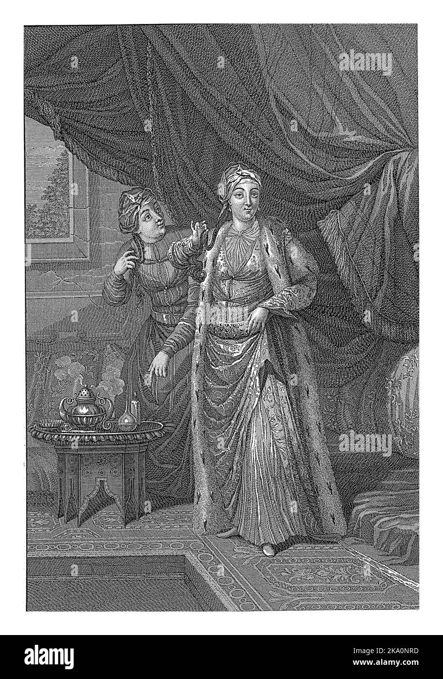 Eine türkische Frau und ihre Magd in traditioneller Kleidung. Das Zimmer, in dem sie sind, ist mit Teppichen bedeckt. Die Magd zeigt die Frau auf einen Tisch auf whi Stockfoto