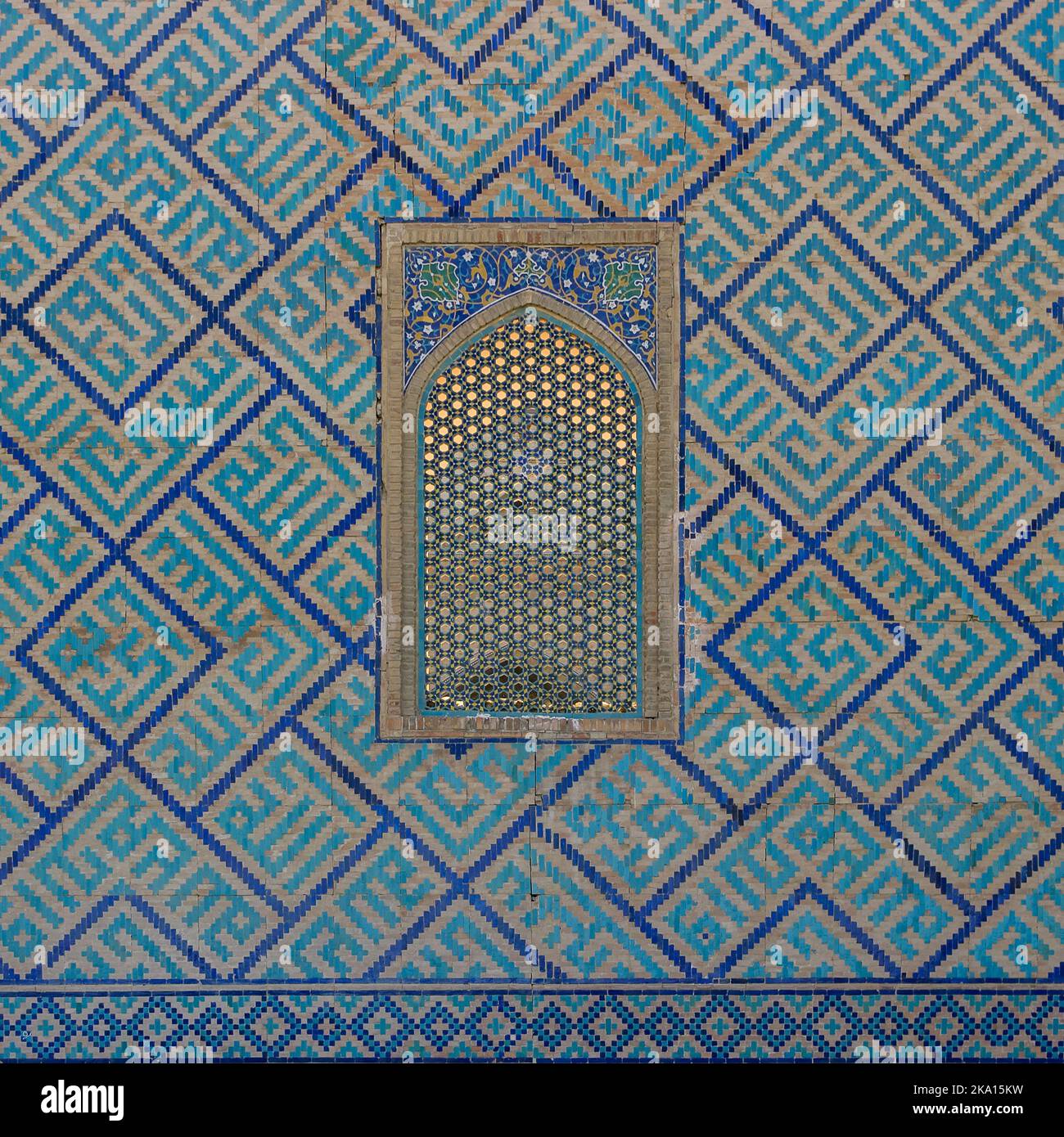 Blaue und türkisfarbene Mosaikdekor und Gitterfenster an der Außenwand von Sher Dor madrassa am historischen Registan-Platz in Samarkand, Usbekistan Stockfoto