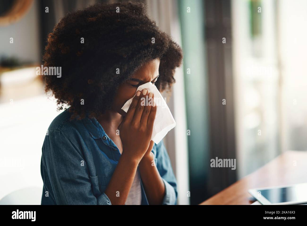 Ich denke, ich fühle eine Grippe. Eine junge Frau bläst ihre Nase, während sie zu Hause arbeitet. Stockfoto