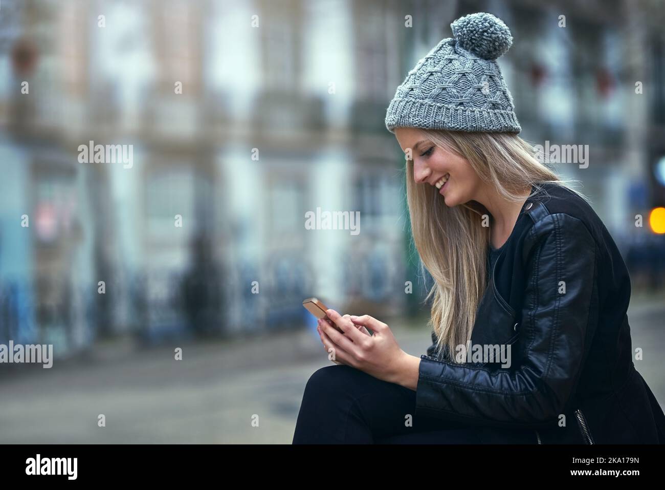 Jeder möchte mit ihr chatten. Eine attraktive Frau, die in der Stadt ein Mobiltelefon benutzt. Stockfoto