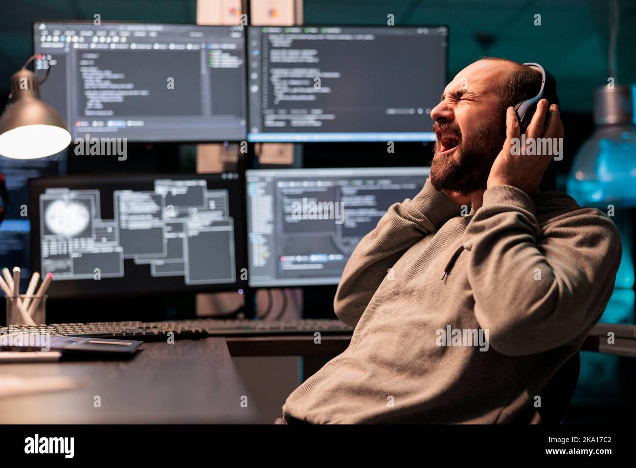 Lustiger Programmierer, der am Headset schreit und Musik hört und spät in der Nacht an der Entwicklung von Software für Anwendungen arbeitet. Web-Entwickler singen Lied im Büro, Codierung Online-Cloud-Datenbank. Stockfoto