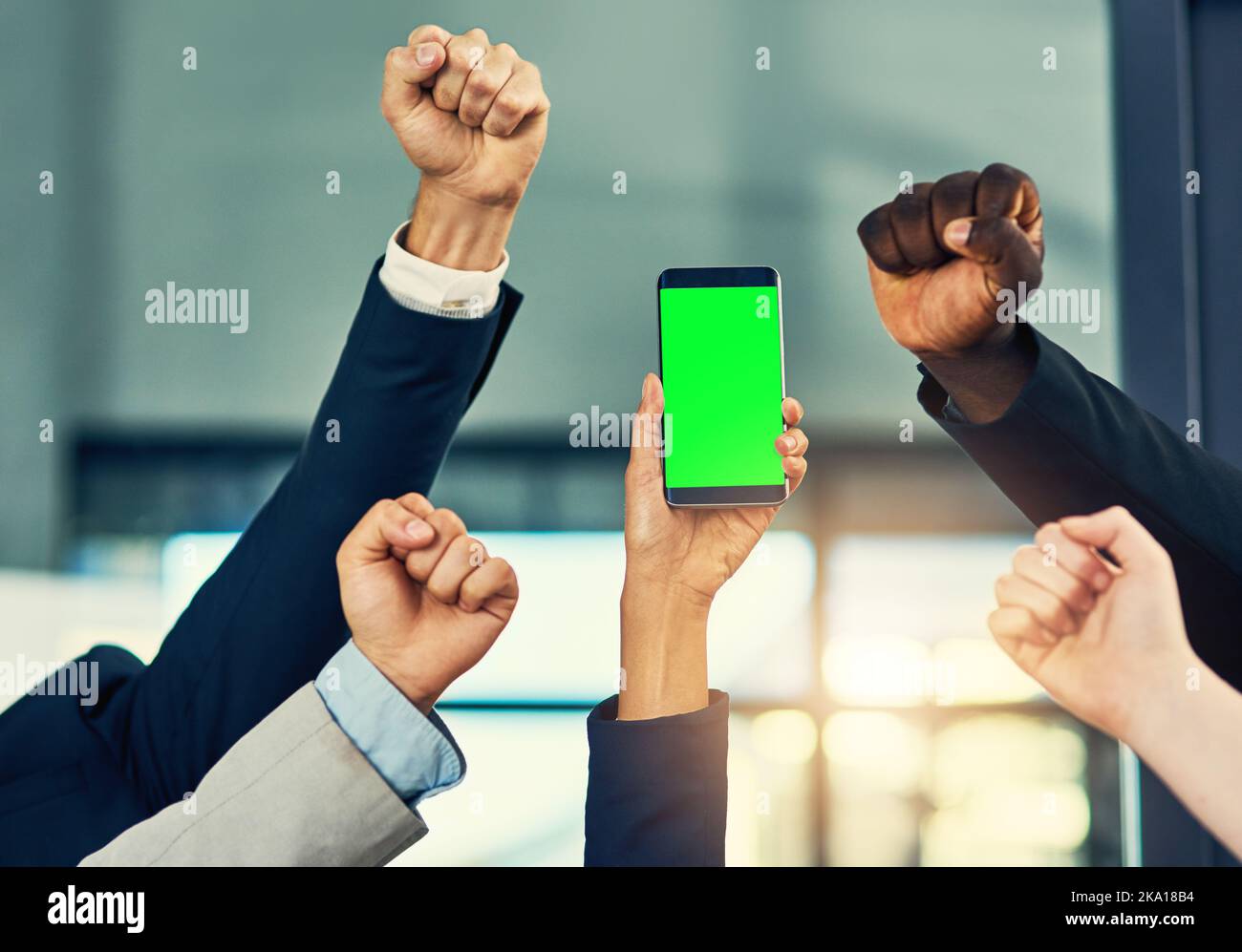 Tun Sie es jetzt, und laden Sie es für Ihr Unternehmen. Eine Gruppe von Geschäftsleuten jubeln und halten ein Mobiltelefon in einem modernen Büro. Stockfoto