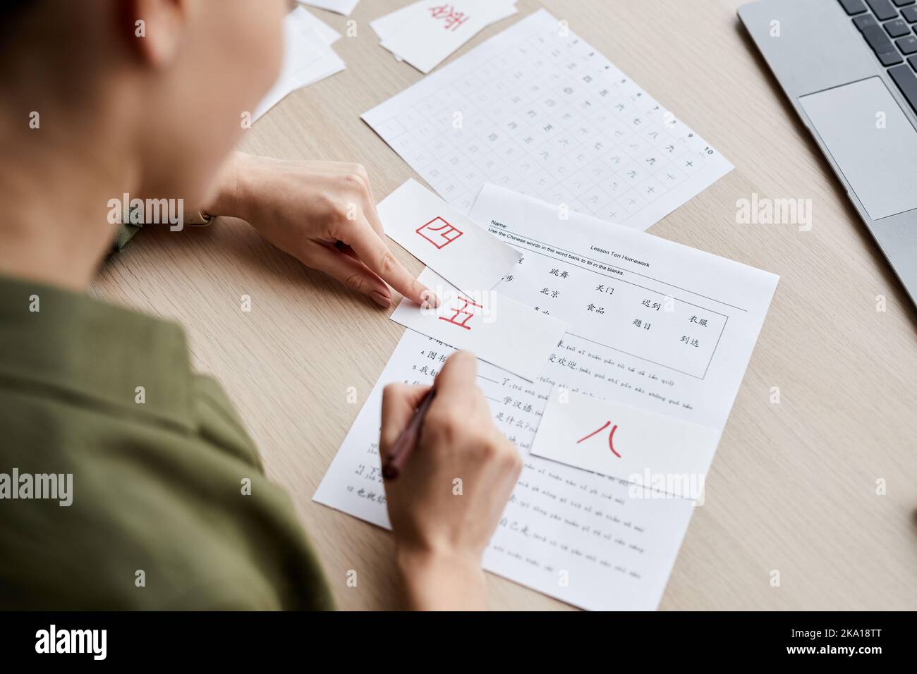 Nahaufnahme einer jungen Frau, die auf die Hieroglyphe zeigt, auf einem auf Papier gedruckten Tisch, während sie alleine Chinesisch studiert Stockfoto