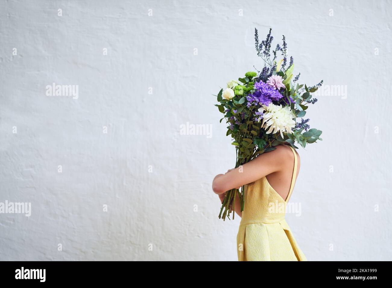 Blumen bringen Glück. Studioaufnahme einer nicht erkennbaren Frau, die einen Blumenstrauß hält, während sie vor einem grauen Hintergrund steht. Stockfoto