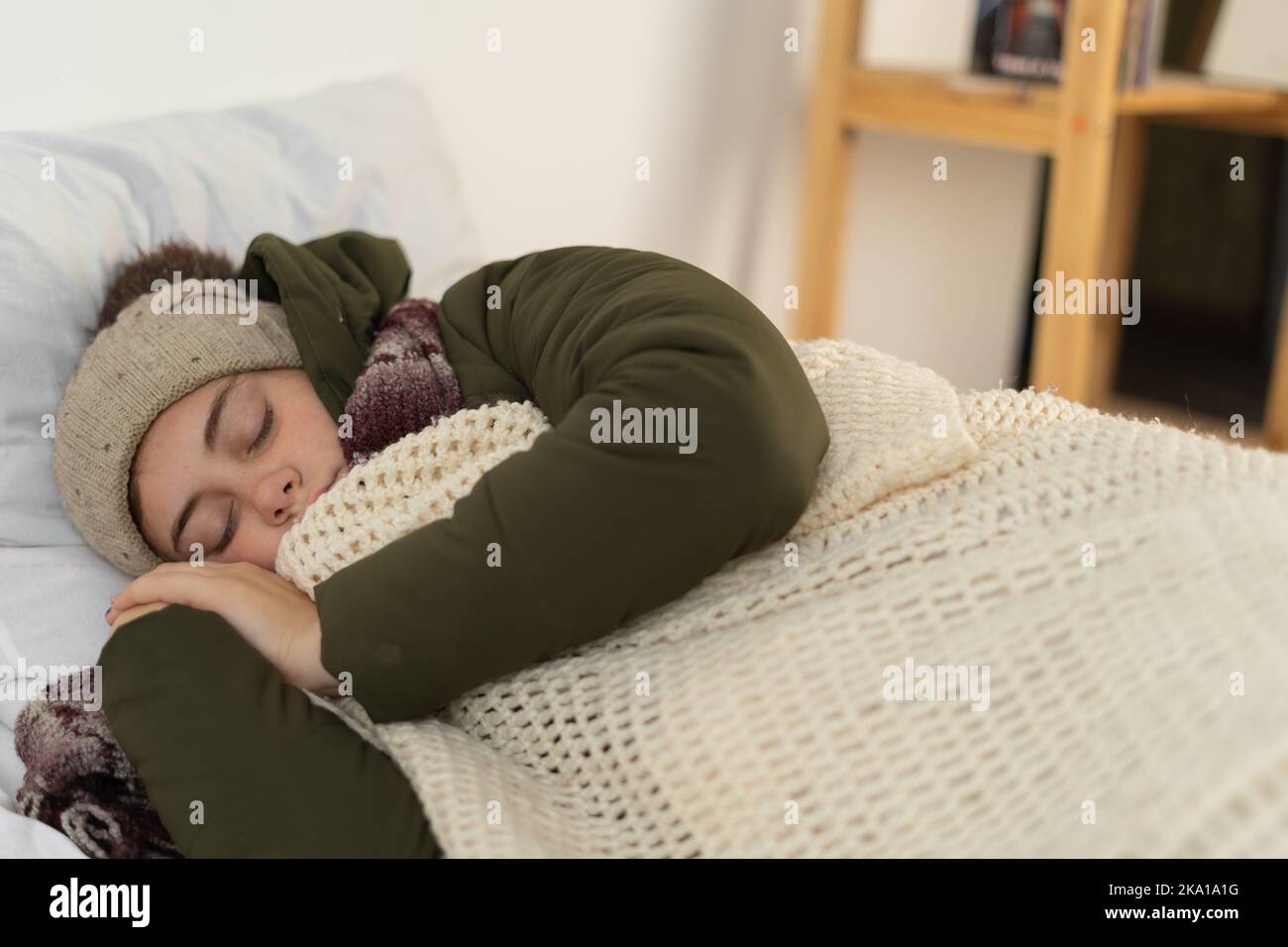 Junge Frau, die in warmen, mit einer Decke bedeckten Kleidern schläft. Kalter Winter. Keine Heizung zu Hause. Keine Heizung Stockfoto