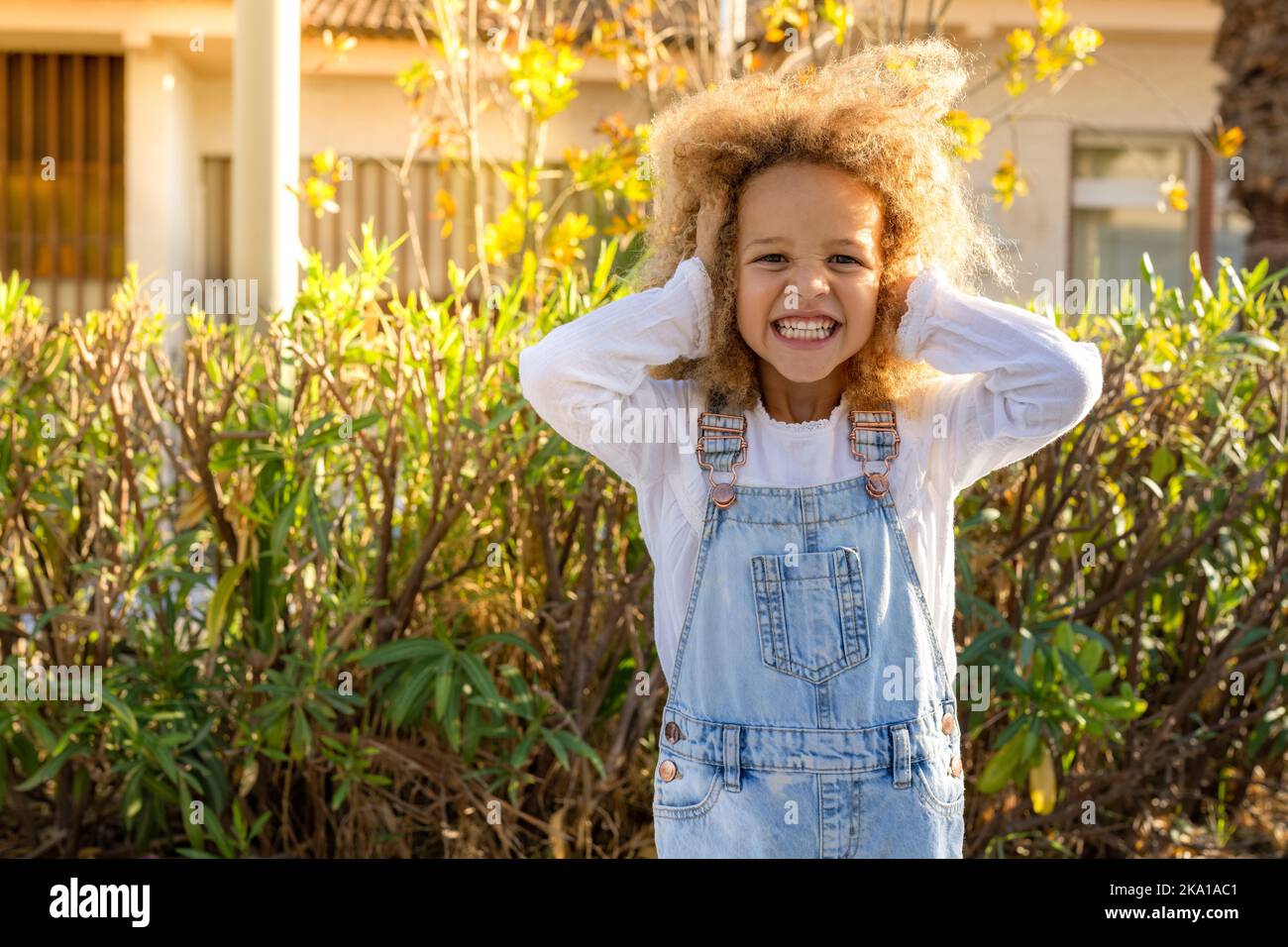 Kleines Mädchen mit lockigen Haaren vor dem Hintergrund des Sommerstadtparks, der ihre Ohren bedeckt. Stockfoto