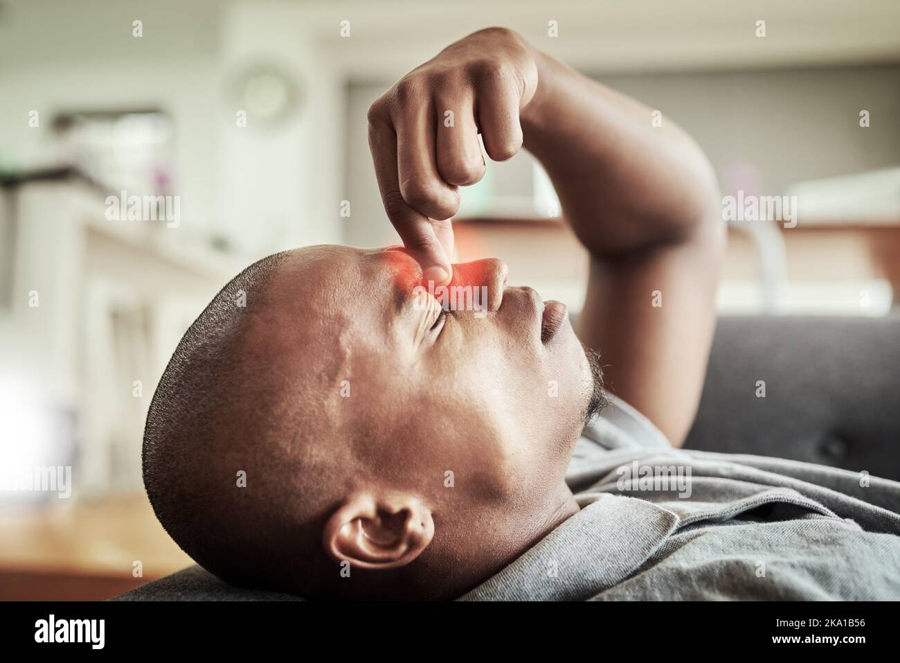 Ich bin nicht in der Stimmung für diesen Tag. Ein gestresster junger Mann liegt auf einer Couch, während er seine Nase in Unannehmlichkeiten drinnen zu Hause während des Tages hält. Stockfoto