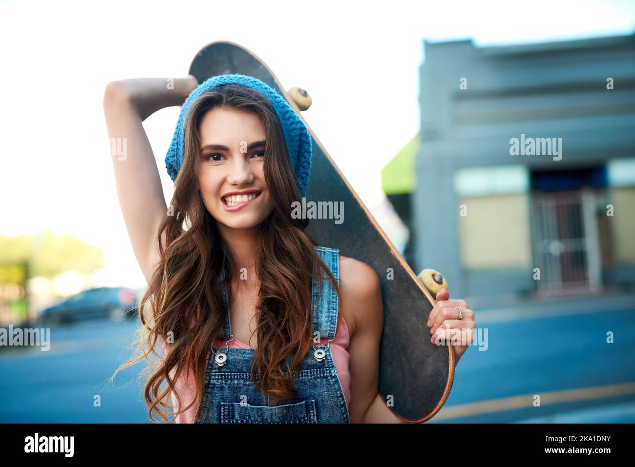 Wo wird sie heute Schlittschuh laufen. Porträt einer attraktiven jungen Skaterin, die tagsüber ein Skateboard hinter ihrem Rücken im Freien hält. Stockfoto