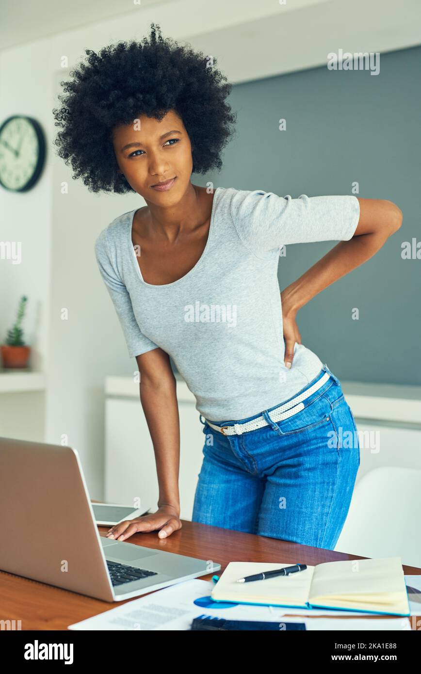 Verdammt, mein Rücken tötet mich. Eine attraktive junge Geschäftsfrau, die unter Rückenschmerzen leidet, während sie zu Hause arbeitet. Stockfoto