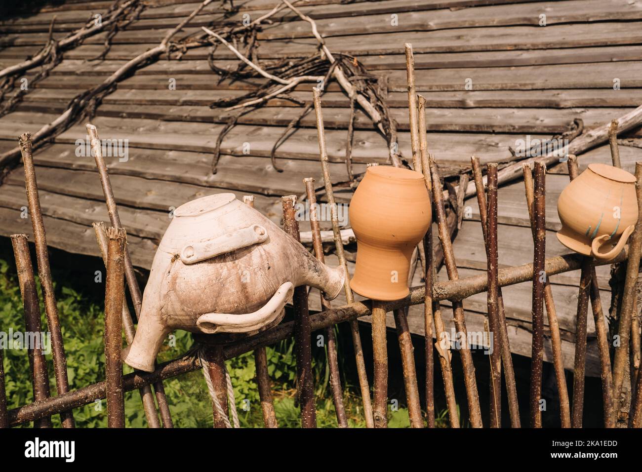 Alte Tontöpfe hängen einfach an einem Weidenzaun. Ukrainische ethnische Gerichte, traditionelle Kultur der Ukraine Stockfoto