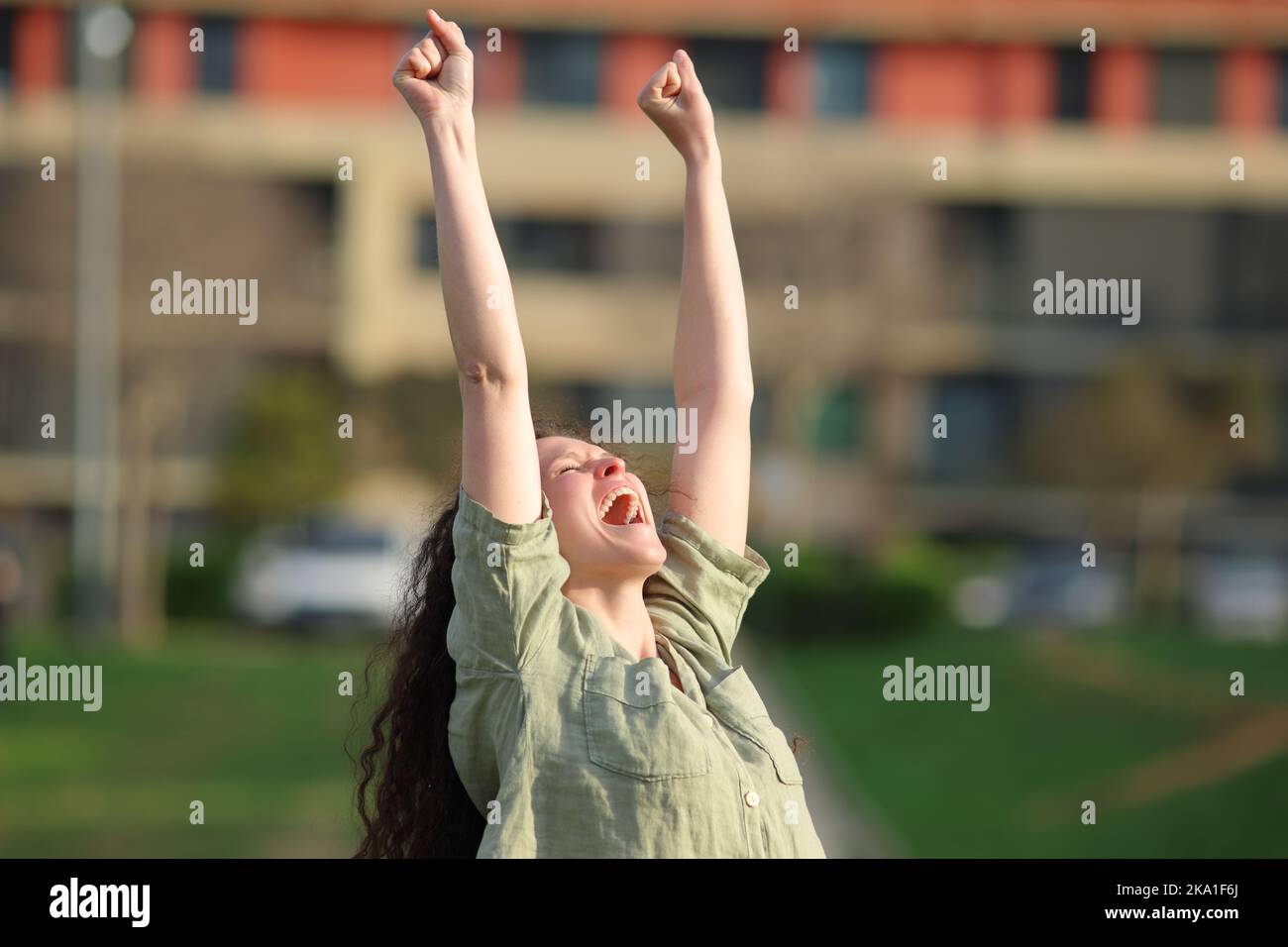 Eine aufgeregte Frau, die den Erfolg feiert und an einem sonnigen Tag die Arme in einem Park hochhebt Stockfoto