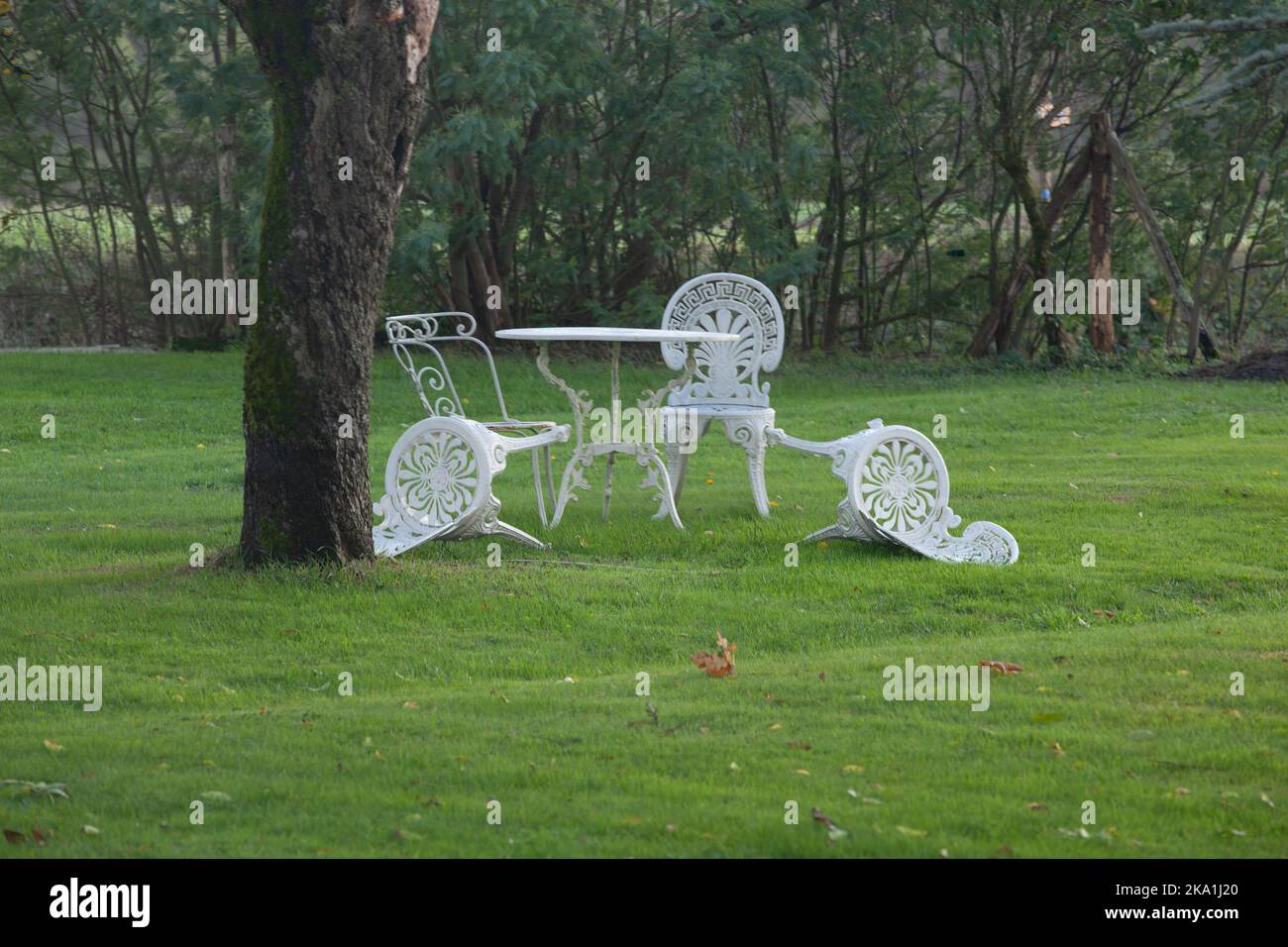 Der Herbstwind schlug zwei der vier weißen Stühle im Garten nieder. Aus diesem Foto entsteht ein Gefühl des Loslassens. Stockfoto