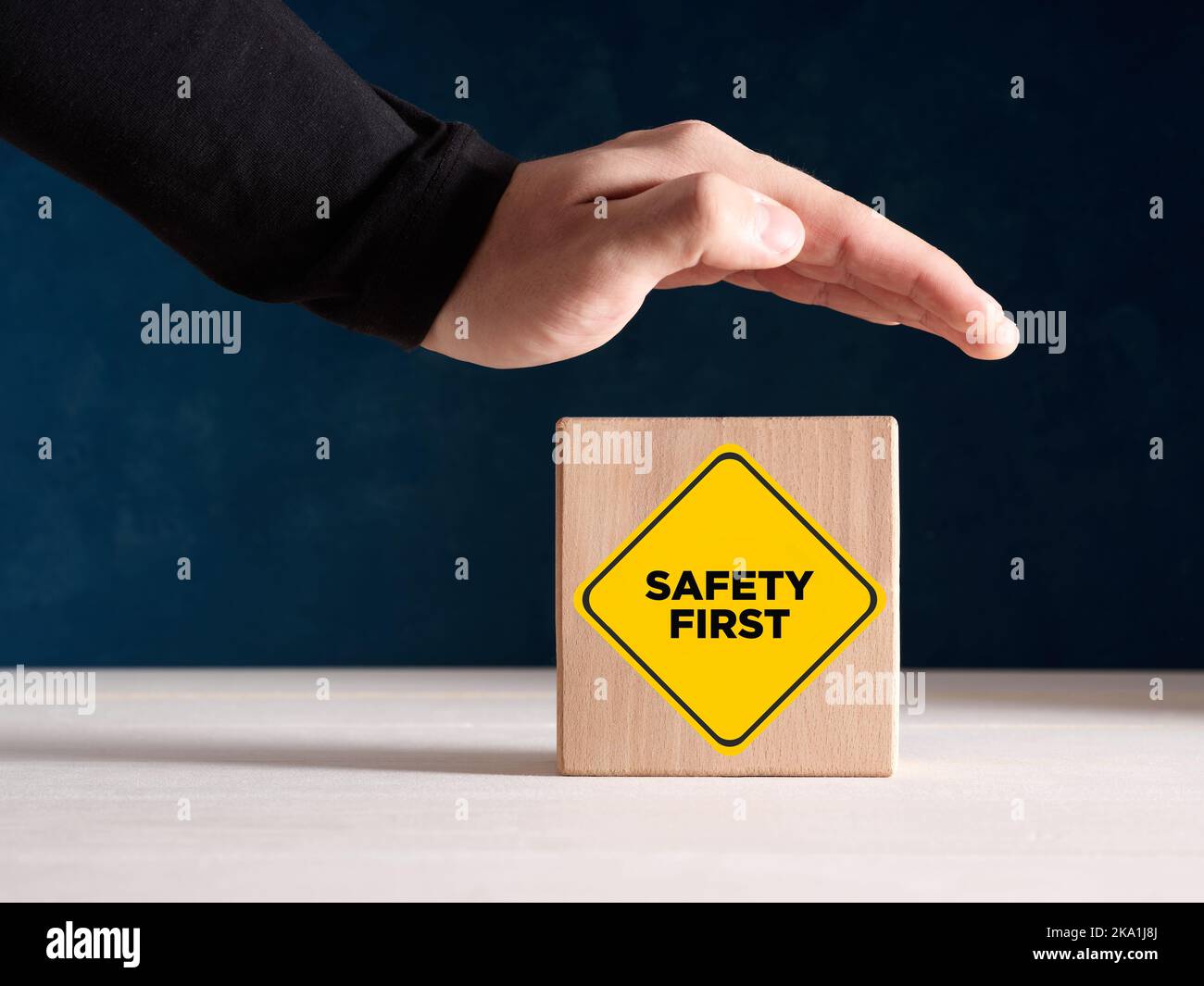 Die männliche Hand steht mit dem Sicherheits-First-Zeichen schützend über dem Holzwürfel. Arbeitssicherheit, Vorsicht, Arbeitsgefahren, Gefahrenüberwachung und Null-Akzide Stockfoto