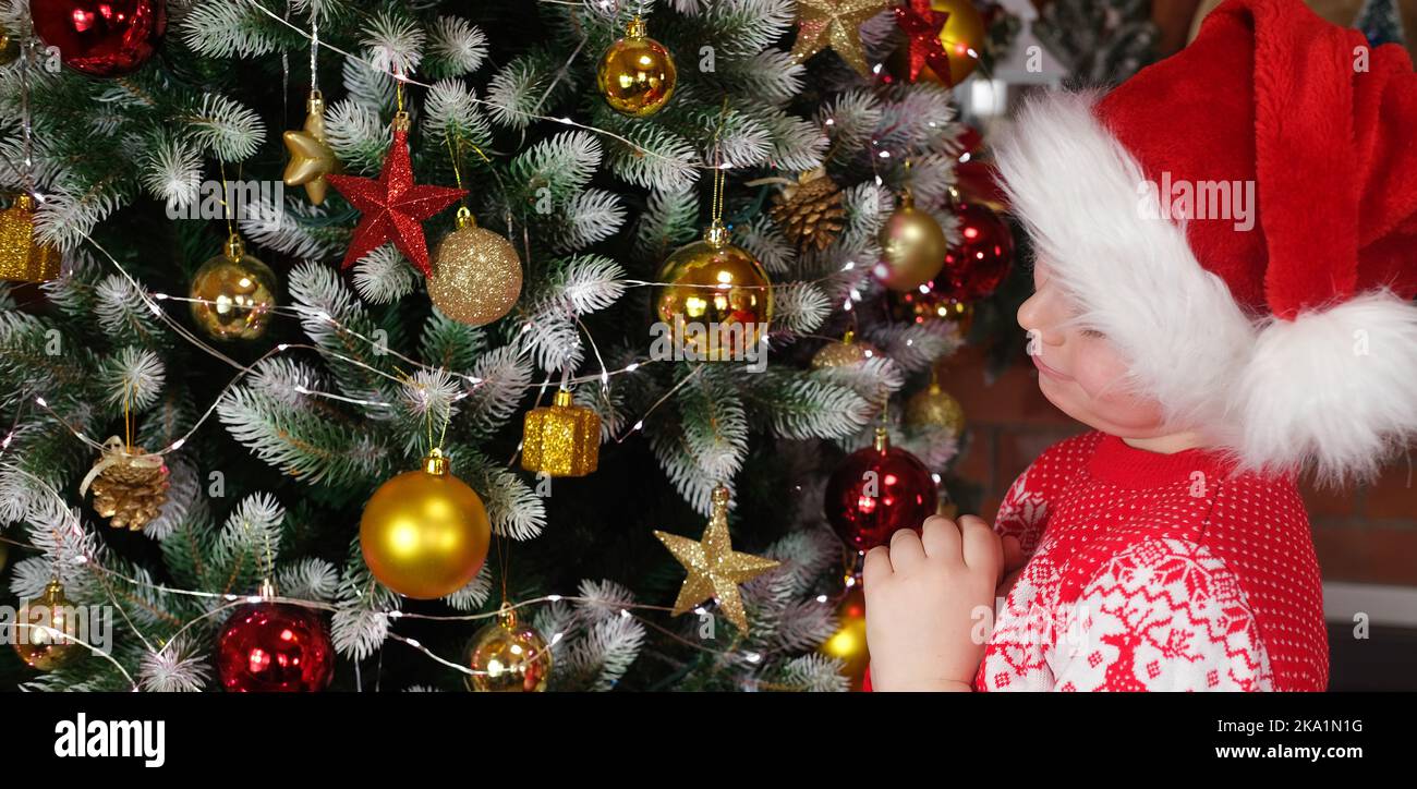 Weihnachten träumt von einem Kind. Frohe Weihnachten Kinder. Ein Junge in einem Weihnachtsmütze, in der Nähe eines Weihnachtsbaums mit Weihnachtslichtern. Stockfoto