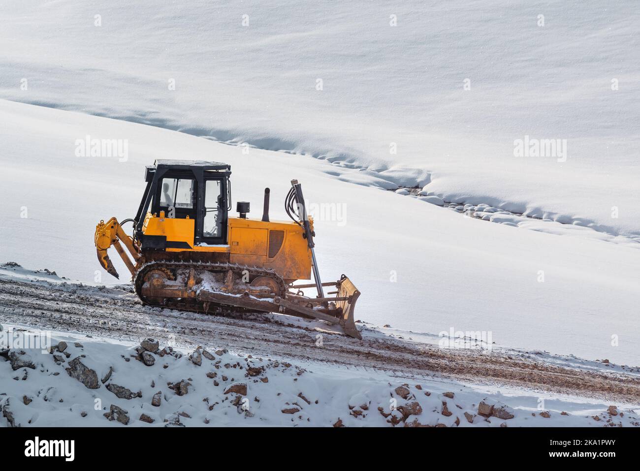 Schwere Straßenbaumaschinen Bulldozer oder Erdbeweger auf der Baustelle auf schneebedeckten Hügel im Winter Stockfoto