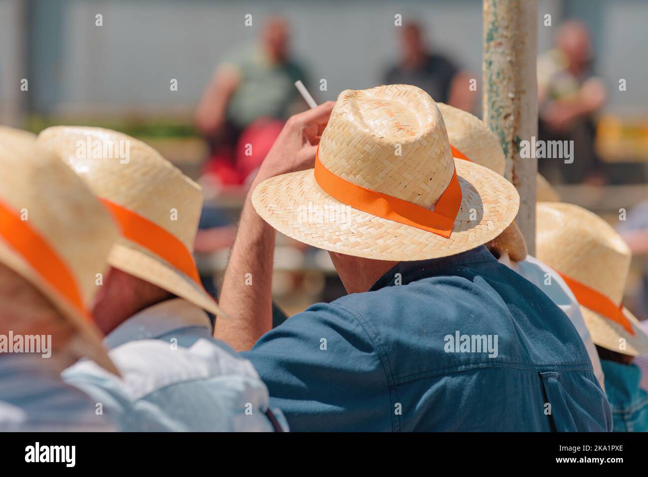 Eine Gruppe von unerkennbaren Gelegenheitsmenschen, die Strohhüte mit orangefarbenem Band tragen, bei einer öffentlichen Veranstaltung mit Reitsport am sonnigen Sommertag, selektiver Fokus Stockfoto