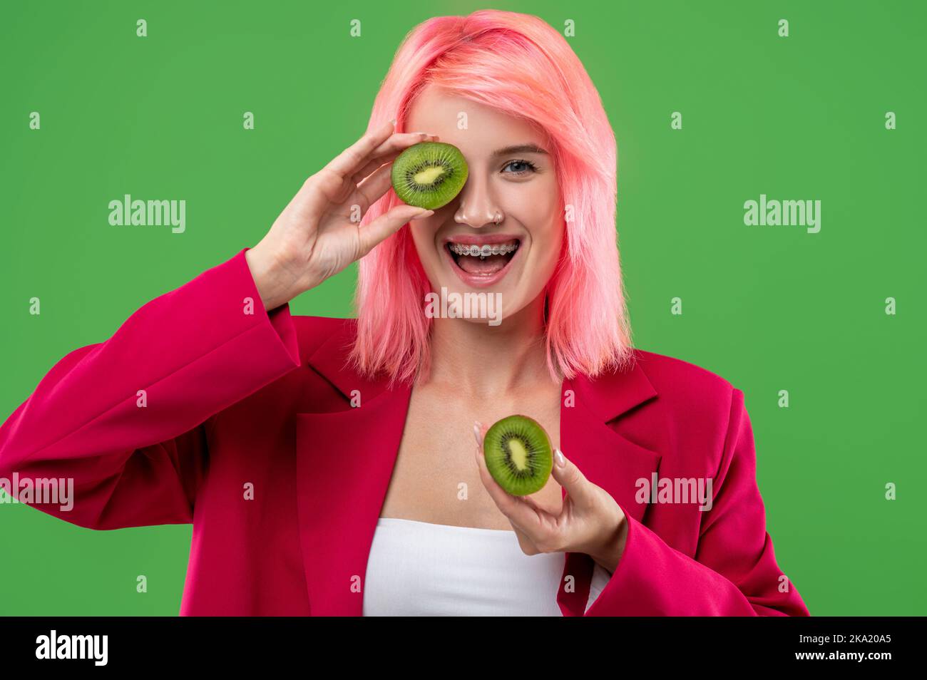 Fröhliches Mädchen posiert mit Kiwifruit vor dem grünen Hintergrund Stockfoto