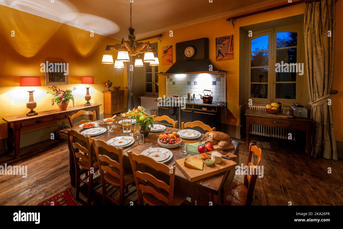 Eine französische Landhausküche mit einem gedeckten Tisch für Gäste, aufgenommen unter atmosphärischer Beleuchtung. Stockfoto