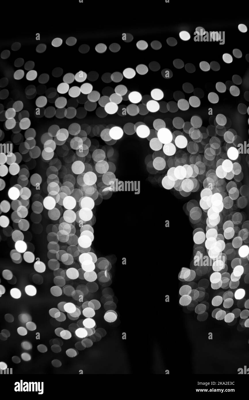 Schwarz-Weiß-Foto, abstrakte Weichzeichnung Bokeh Hintergrund mit einer Silhouette von Frau. Einsamer Mensch allein unter den festlichen Weihnachtslichtern. Belastung, Abschr Stockfoto