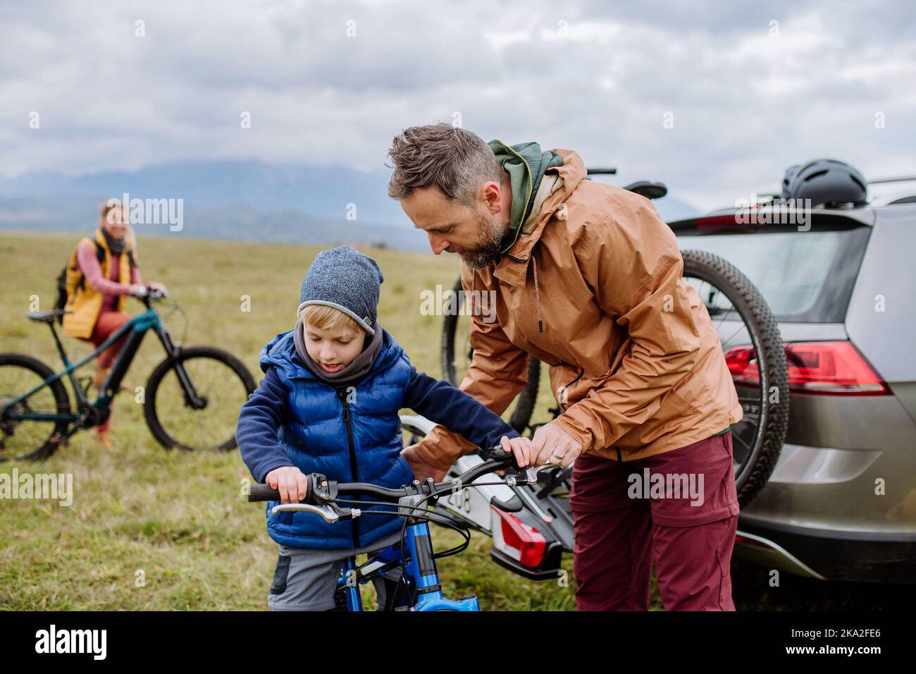 Junge Familie mit kleinen Kindern, die sich auf eine Fahrradtour in der Natur vorbereiten und Fahrräder von den Autoabstellern abstellen. Gesundes Lifestyle-Konzept. Stockfoto