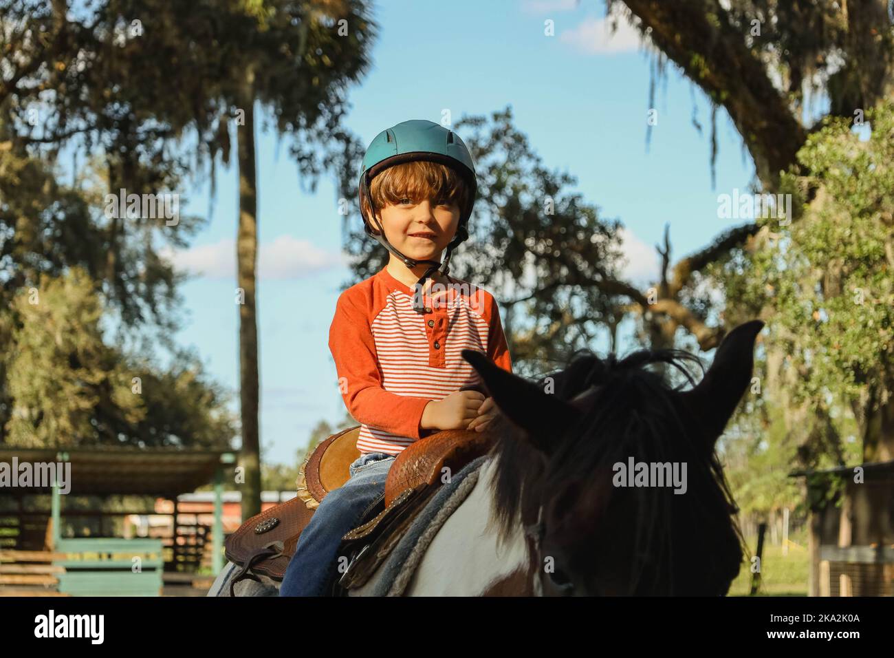 Ein kaukasischer Junge mit Helm und Reitpferd im Grünen Stockfoto