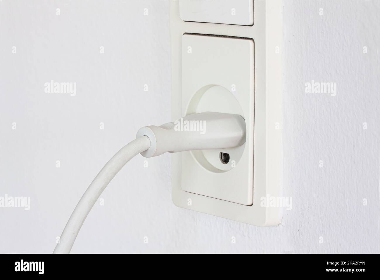 Nahaufnahme des Steckers eines elektrischen Geräts, das an eine Steckdose auf einem weißen Wandhintergrund angeschlossen ist. Steckdose weiß mit Kabel. Strom Stockfoto