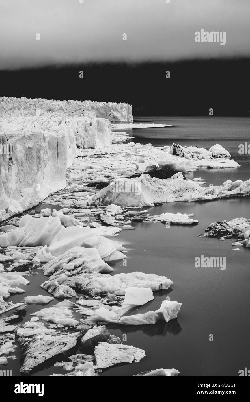 Eine vertikale Graustufenaufnahme von Gletschern im Wasser in der Nähe von schneebedeckten Bergen in El Calafate, Argentinien Stockfoto