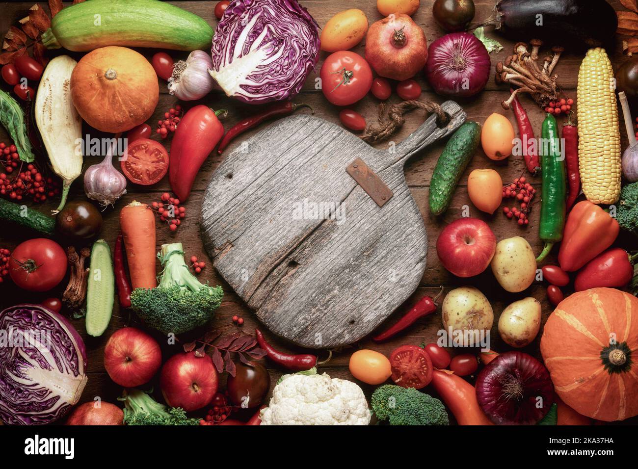Ein leeres Vintage Schneidebrett auf einem Tisch mit Obst und Gemüse. Gesundes Essen und vegane Rezepte retro rustikale Fotografie. Stockfoto