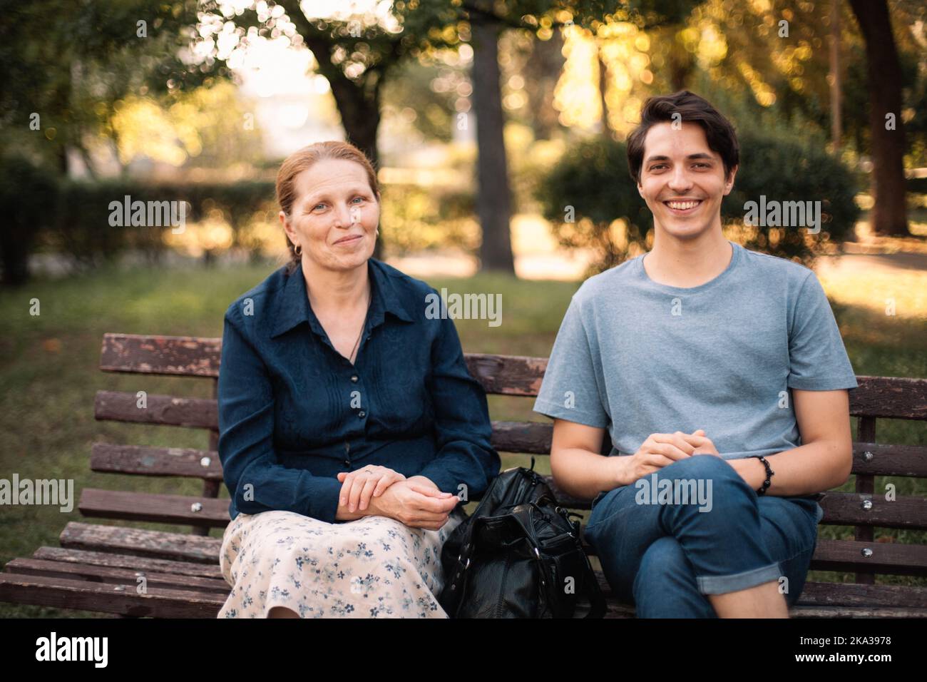 Glückliche, reife Mutter und lächelnder, erwachsener Sohn sitzen auf der Bank im Park Stockfoto