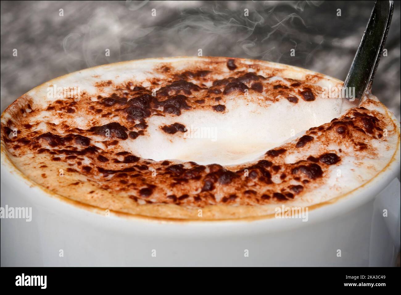 Cappuccino mit gemahlener Schokolade, die in heißem Milchschaum in einem weißen Becher mit Löffel geschmolzen ist. Schwarz-Weiß-Hintergrundumwandlung und zusätzlicher Dampfeffekt Stockfoto