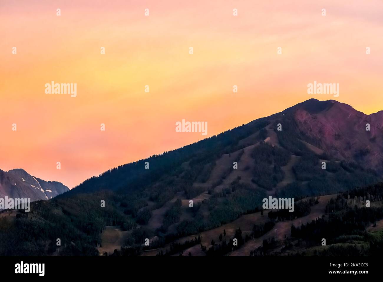 Der pastellorange Sonnenuntergang in Aspen, Colorado, mit dem Gipfel der felsigen Berge im Herbst und der leuchtend gelben Farbe in der Dämmerung über dem Buttermilch-Skigebiet Stockfoto